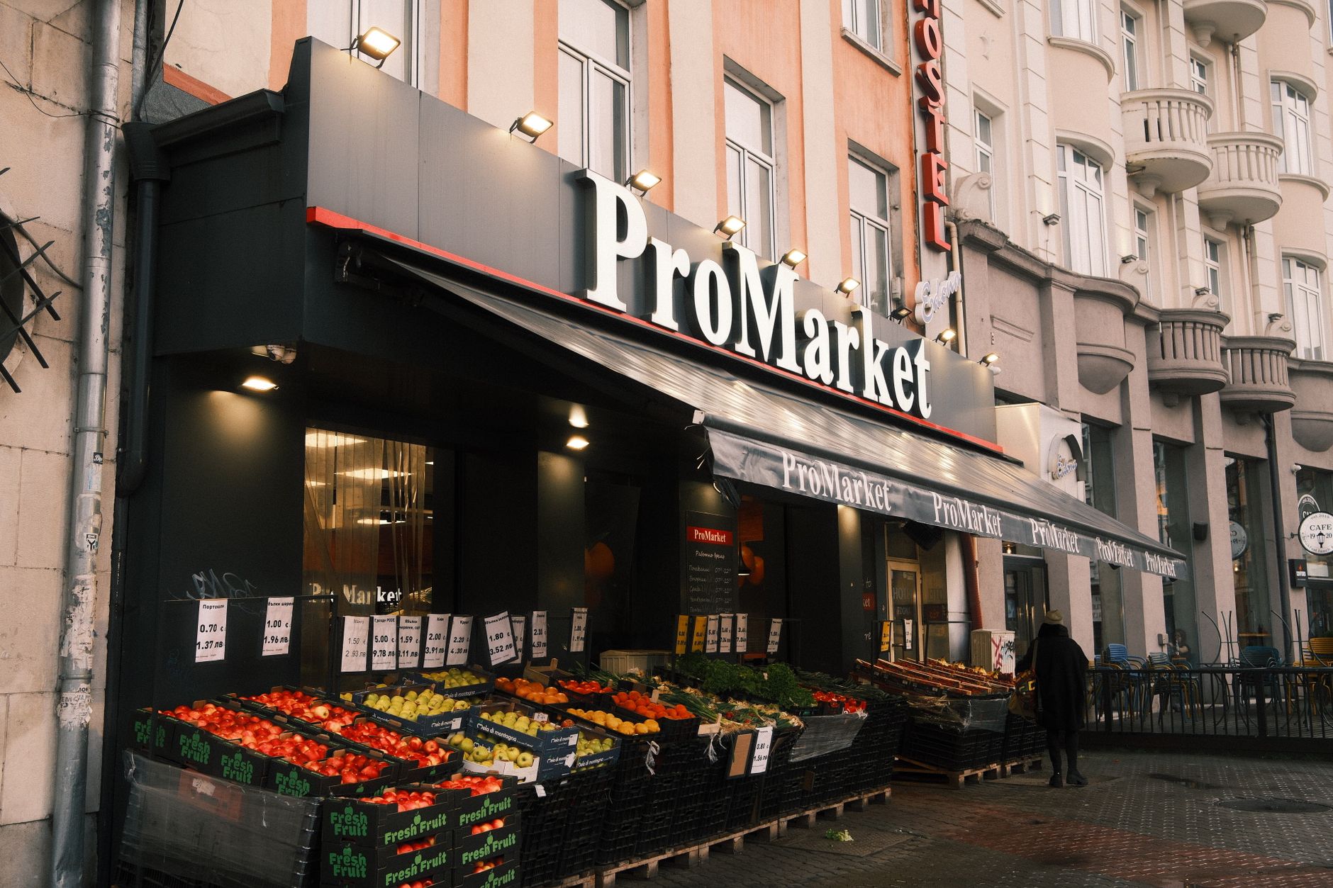Photo of an urban grocery store, ProMarket, displaying colorful fresh produce outside.