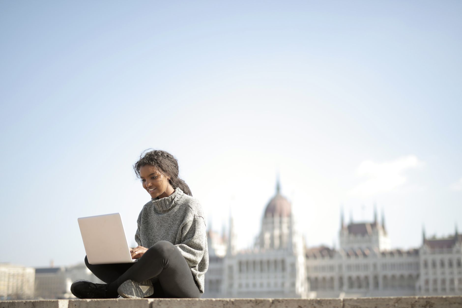 Woman working on laptop in front of Budapest's Parliament Building, enjoying outdoor remote work.