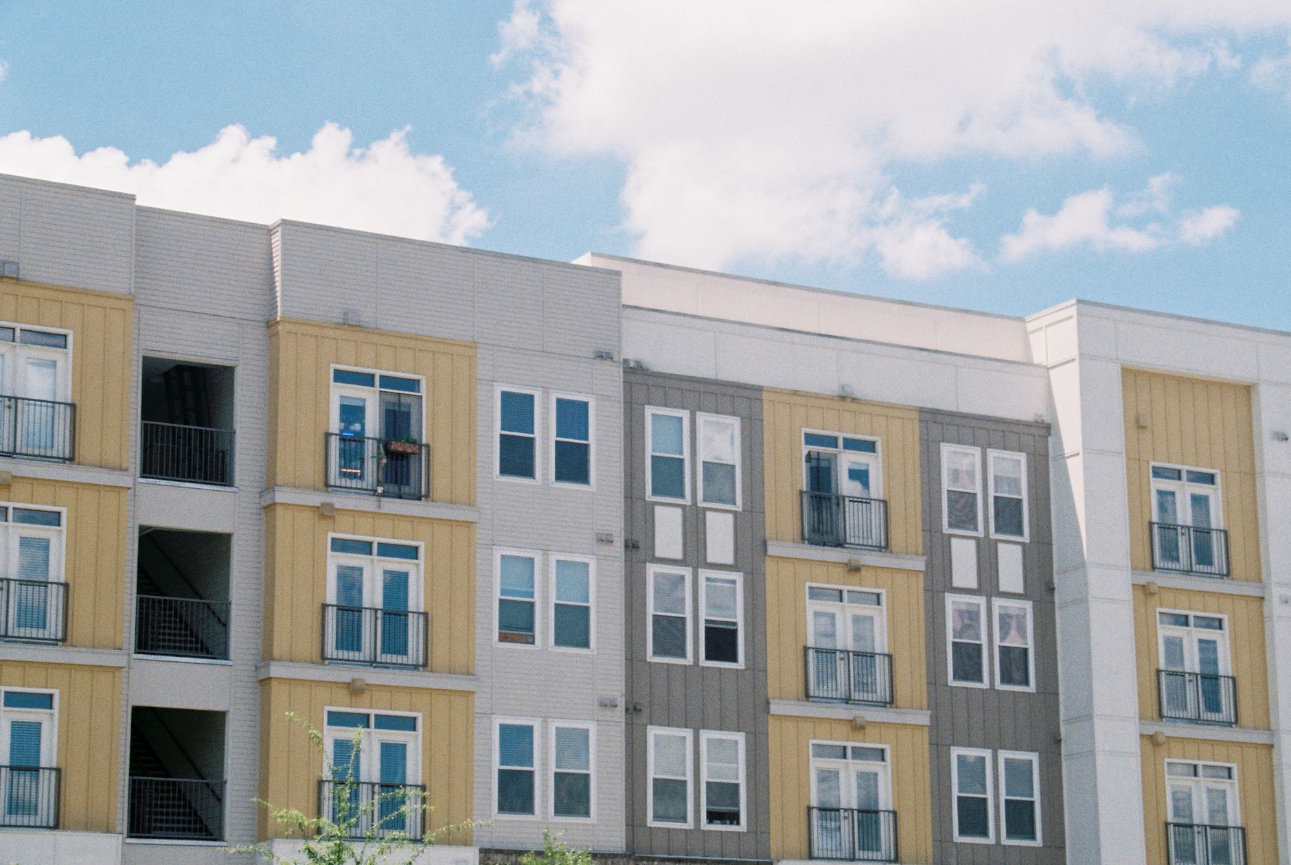 Contemporary apartment building exterior with yellow and grey panels under a clear blue sky.