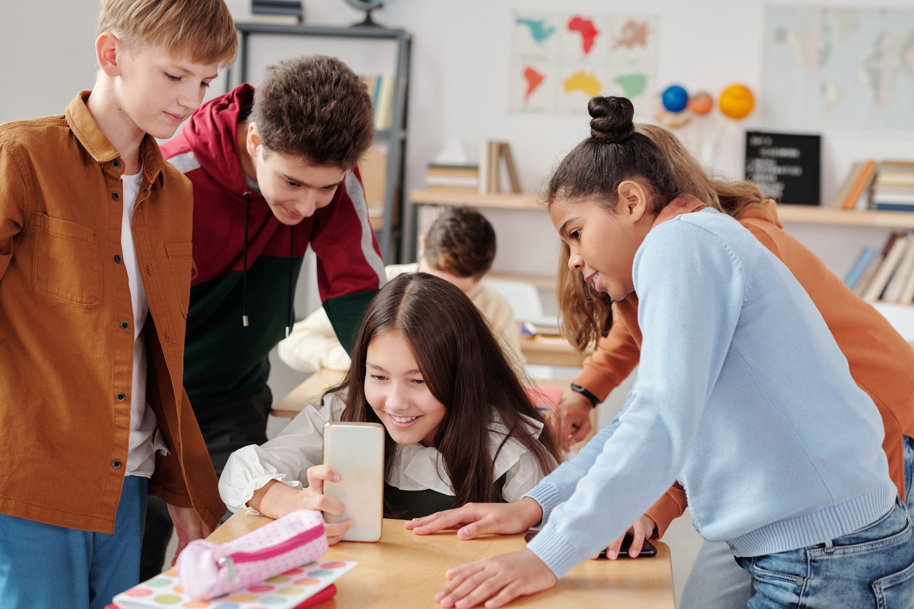 Group of teenagers engaging with a smartphone in a lively classroom environment.