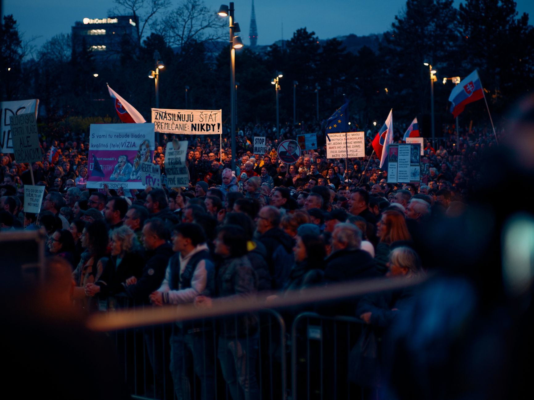 A large peaceful protest in Bratislava, Slovakia, featuring signs and flags during the night.