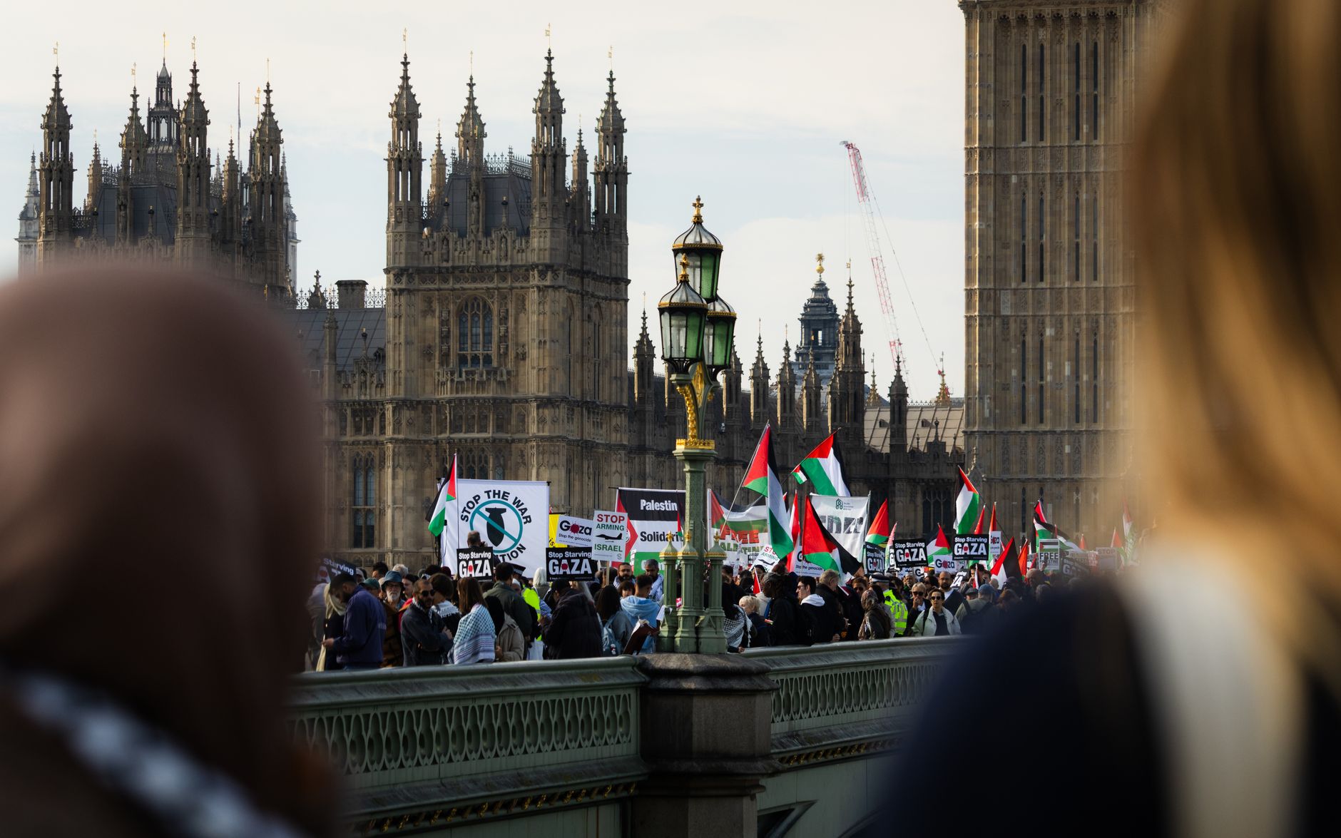 Crowd protesting on Westminster Bridge, London against Gaza conflict, waving Palestinian flags.