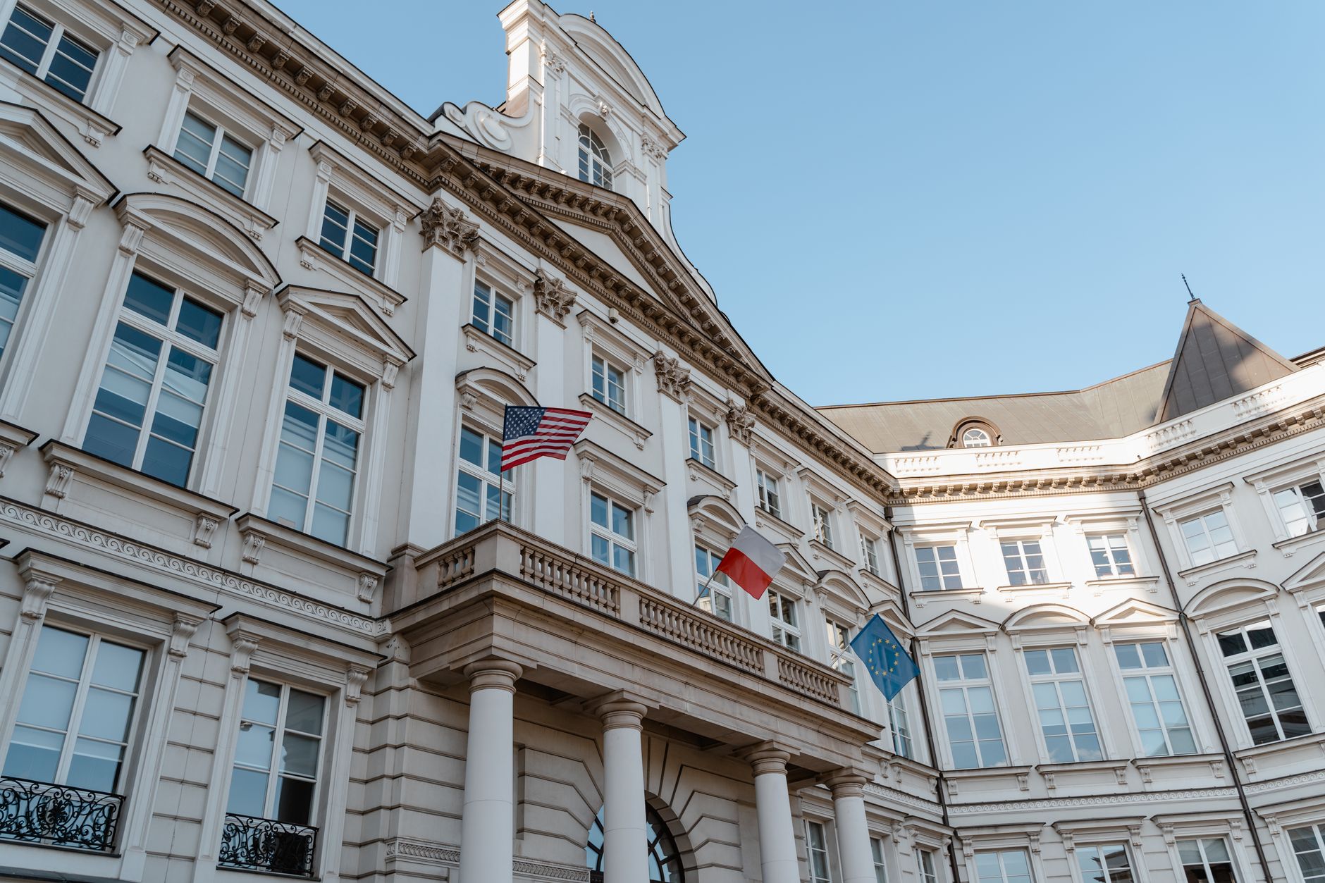 Low angle shot of a historic building with flags in an urban European district.