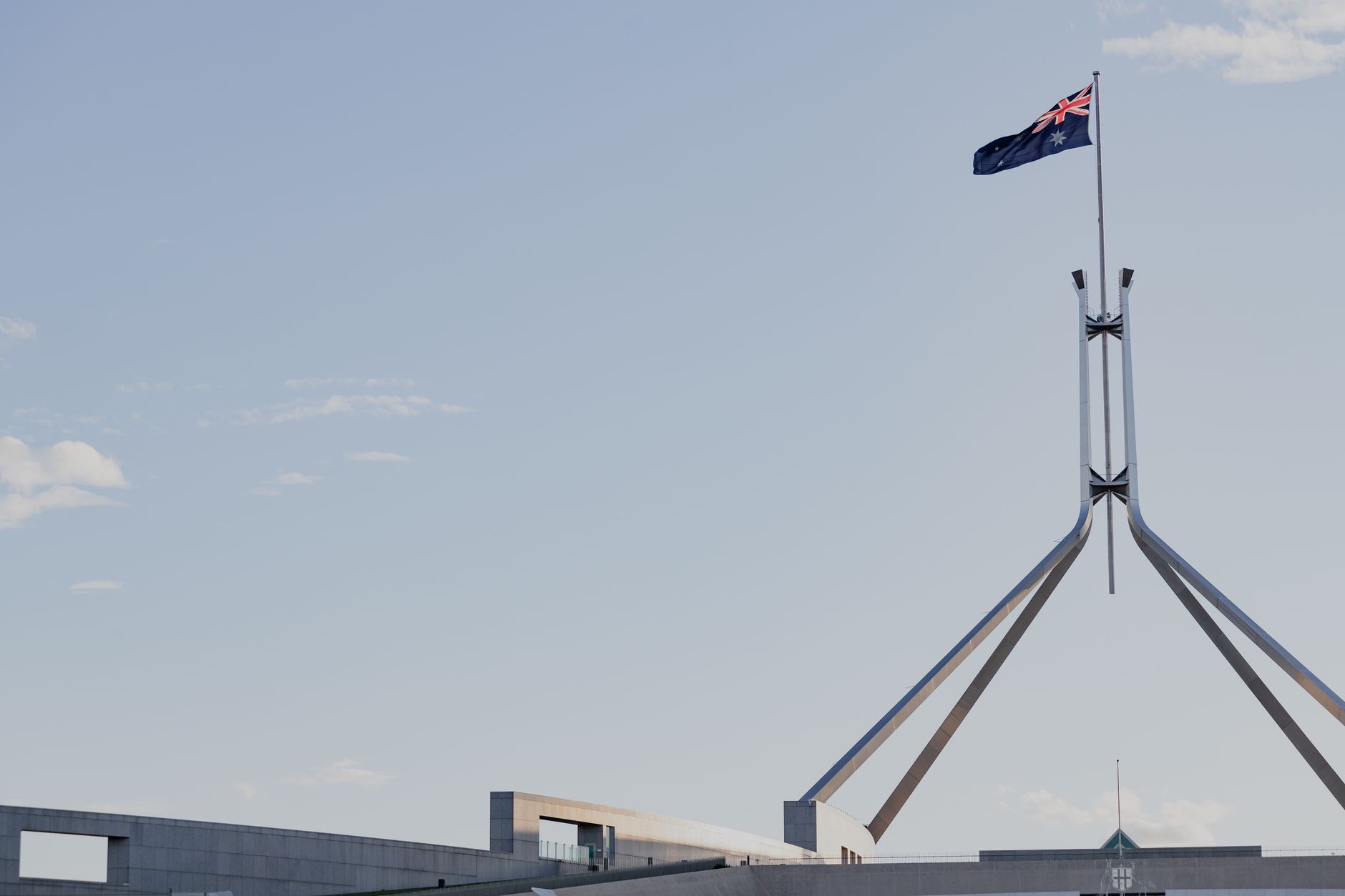 Canberra's iconic Australian Parliament House with national flag against a clear blue sky.