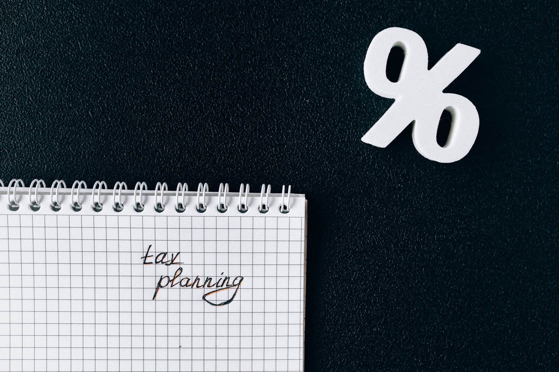 A notebook with 'tax planning' written on a grid paper next to a percent symbol on a black background.