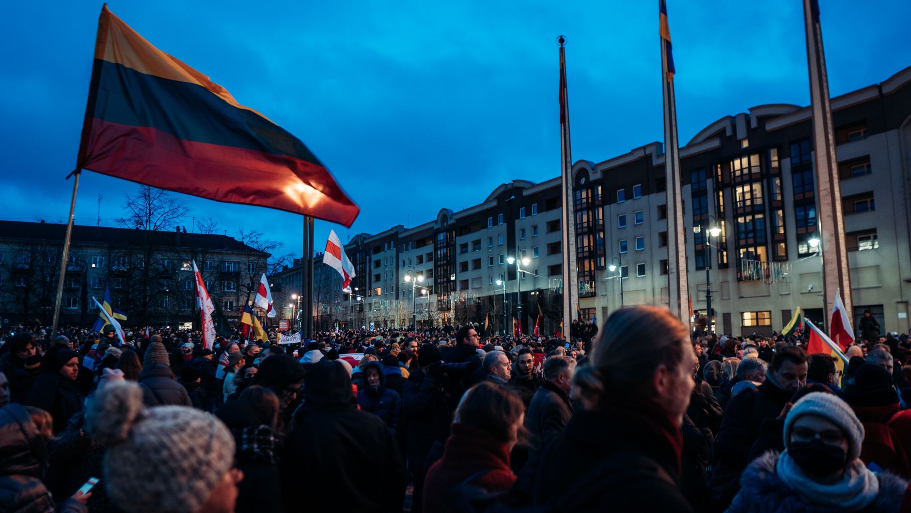 A large crowd gathers at dusk in Vilnius, Lithuania, waving flags during a peaceful protest.