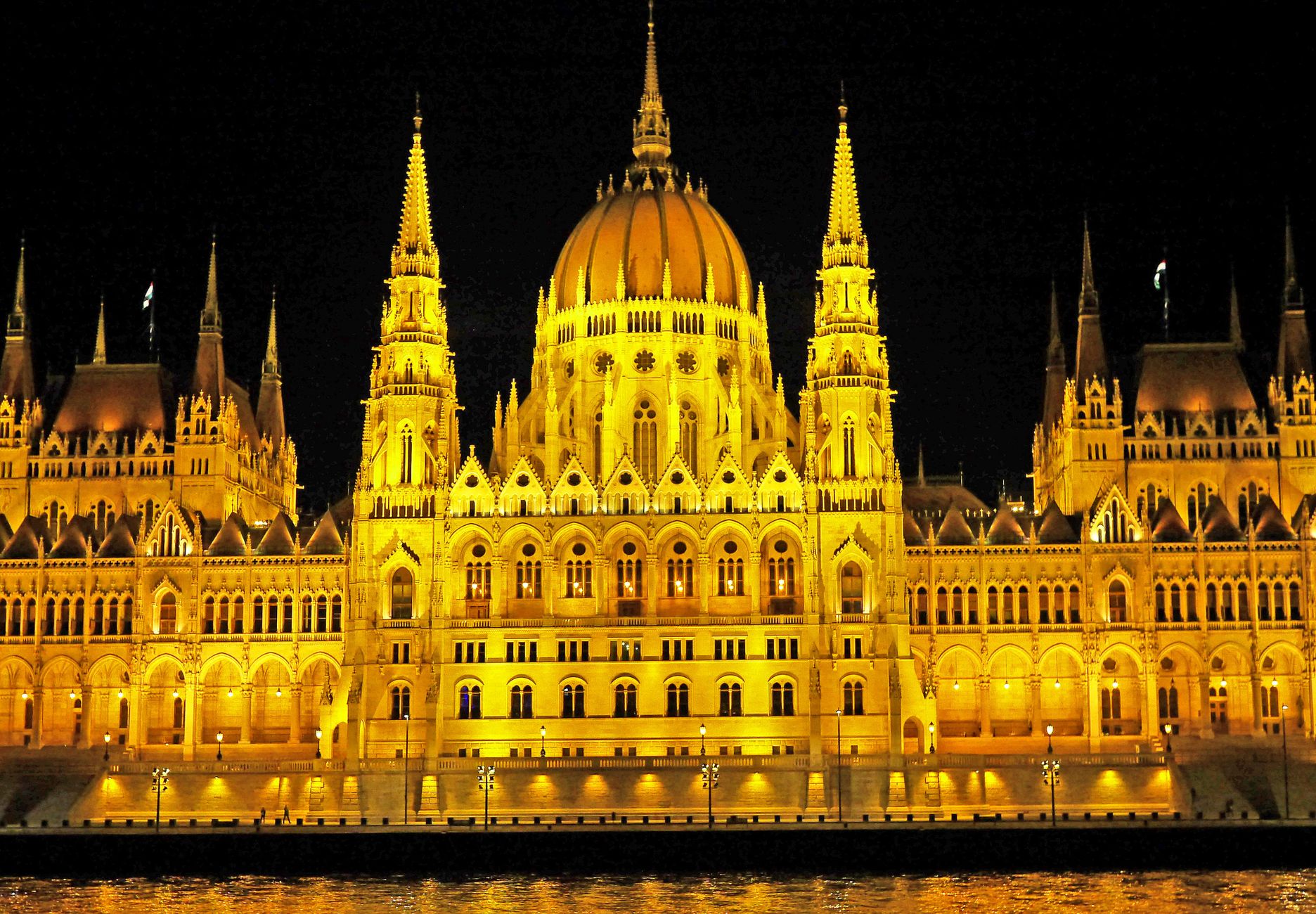 Illuminated Hungarian Parliament Building with reflection on Danube River at night.