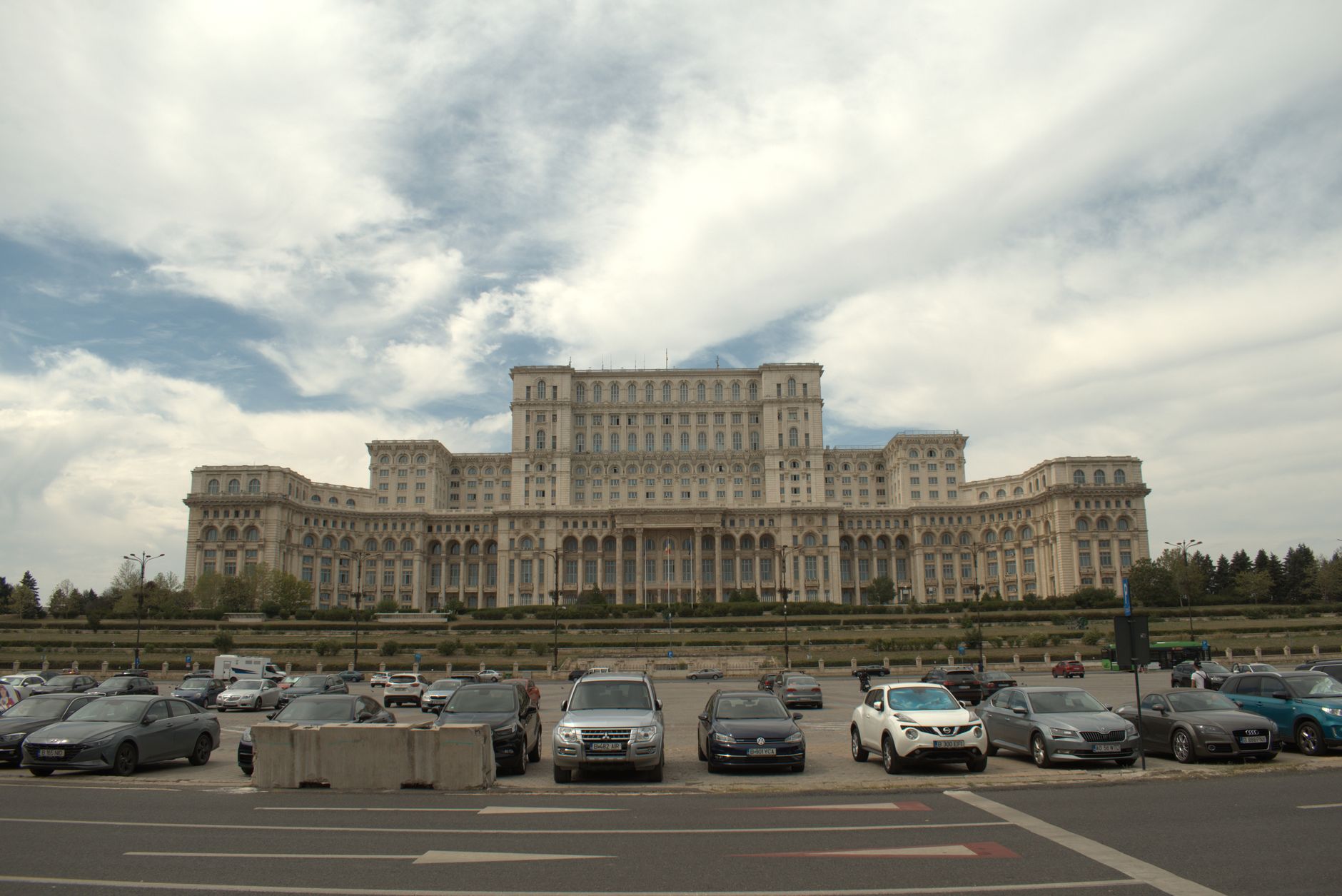 A daytime view of the iconic Palace of the Parliament in Bucharest, Romania, featuring the grand architecture and parked cars.