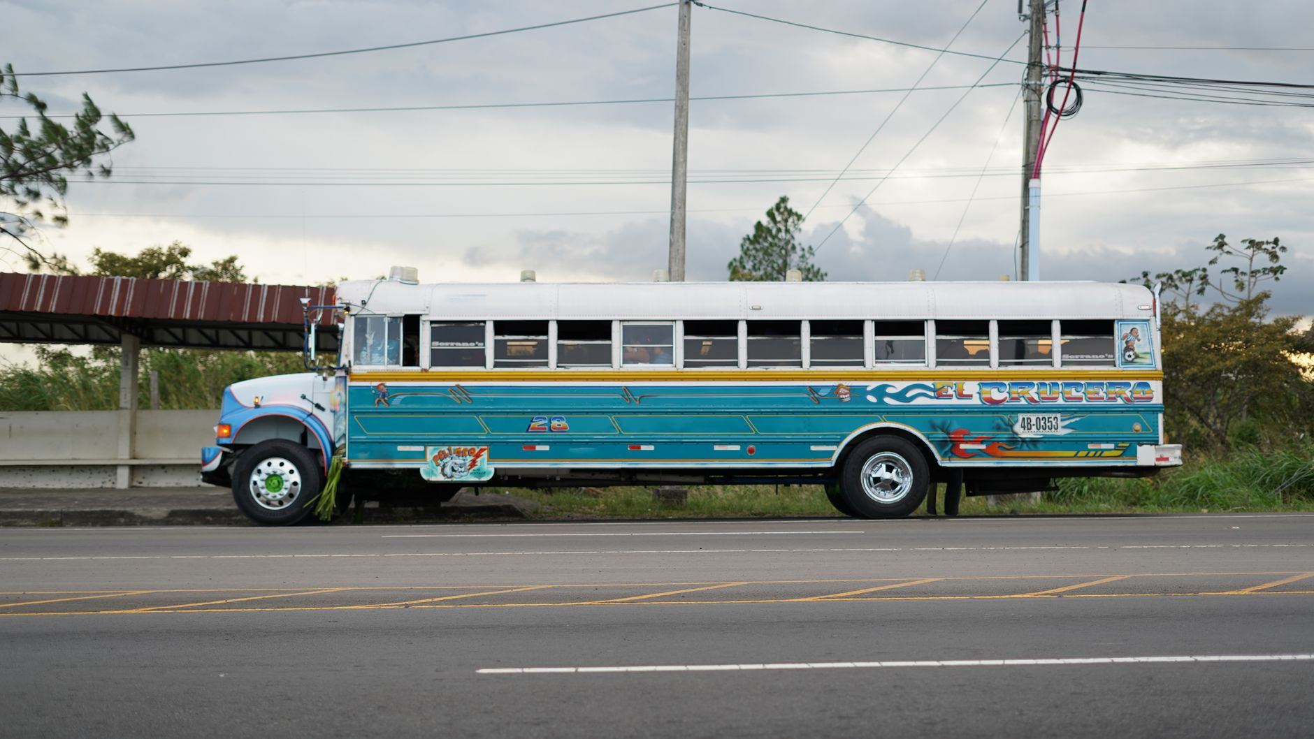 Colorful blue school bus parked by the roadside with cloudy sky backdrop.