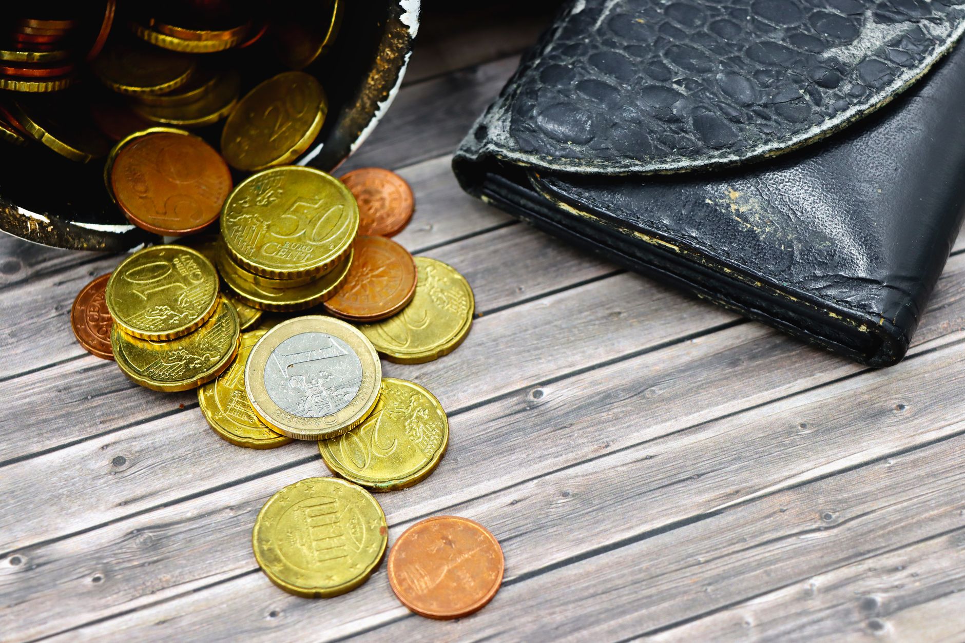 A worn-out leather wallet and scattered euro coins on wooden surface suggest economic hardship.
