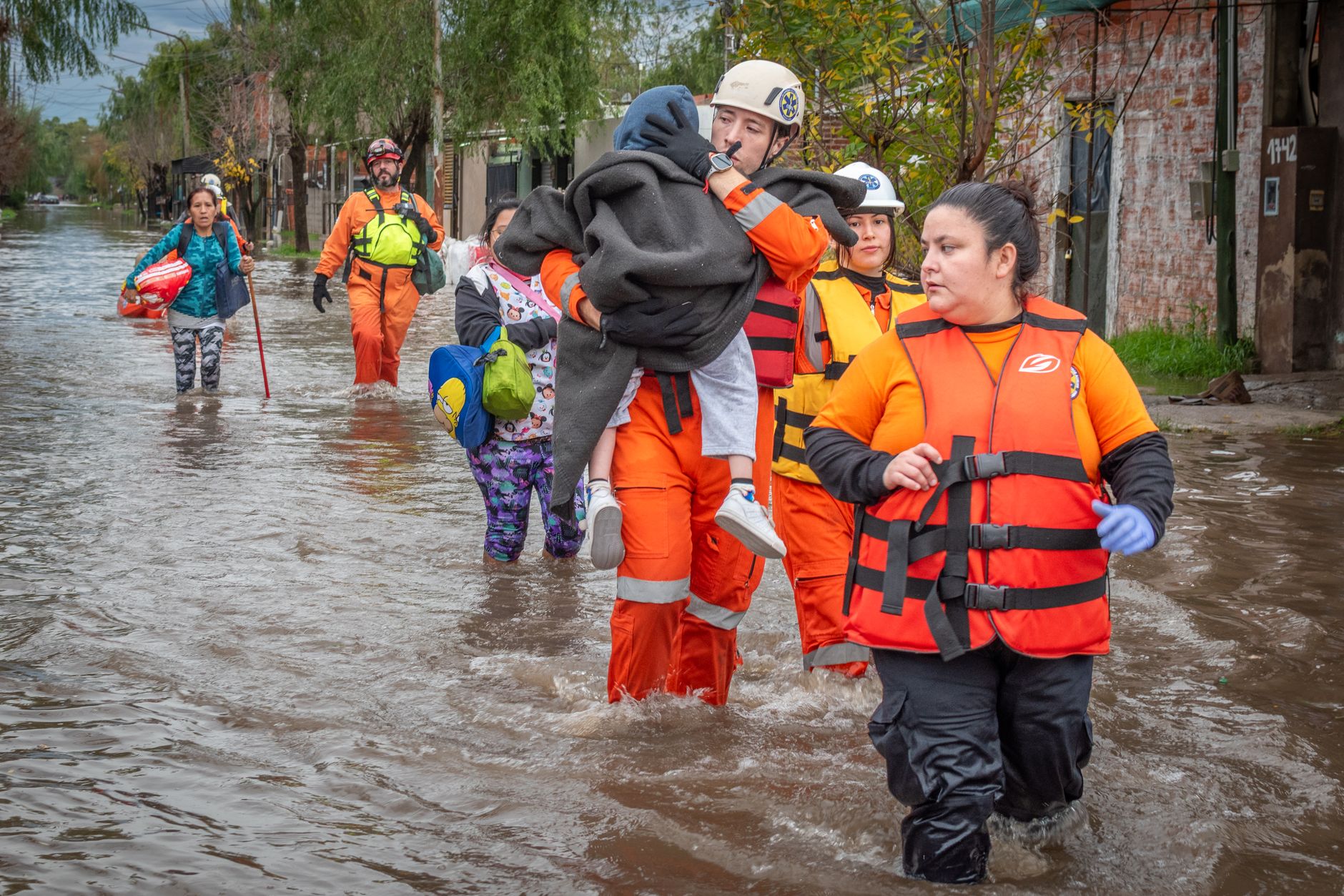 Rescue workers in orange gear helping people during a flood, showcasing bravery and teamwork.