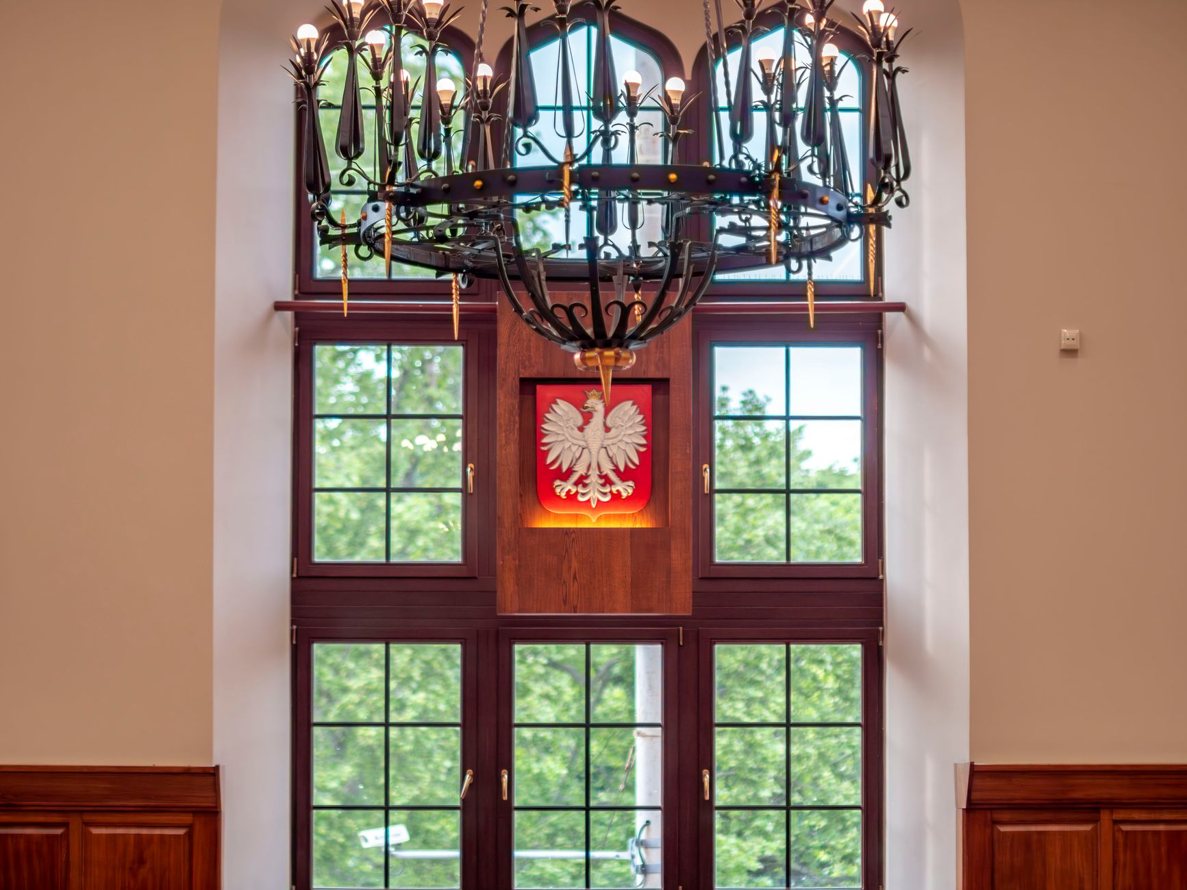 Window with Polish emblem in elegant interior, featuring a stylish chandelier.