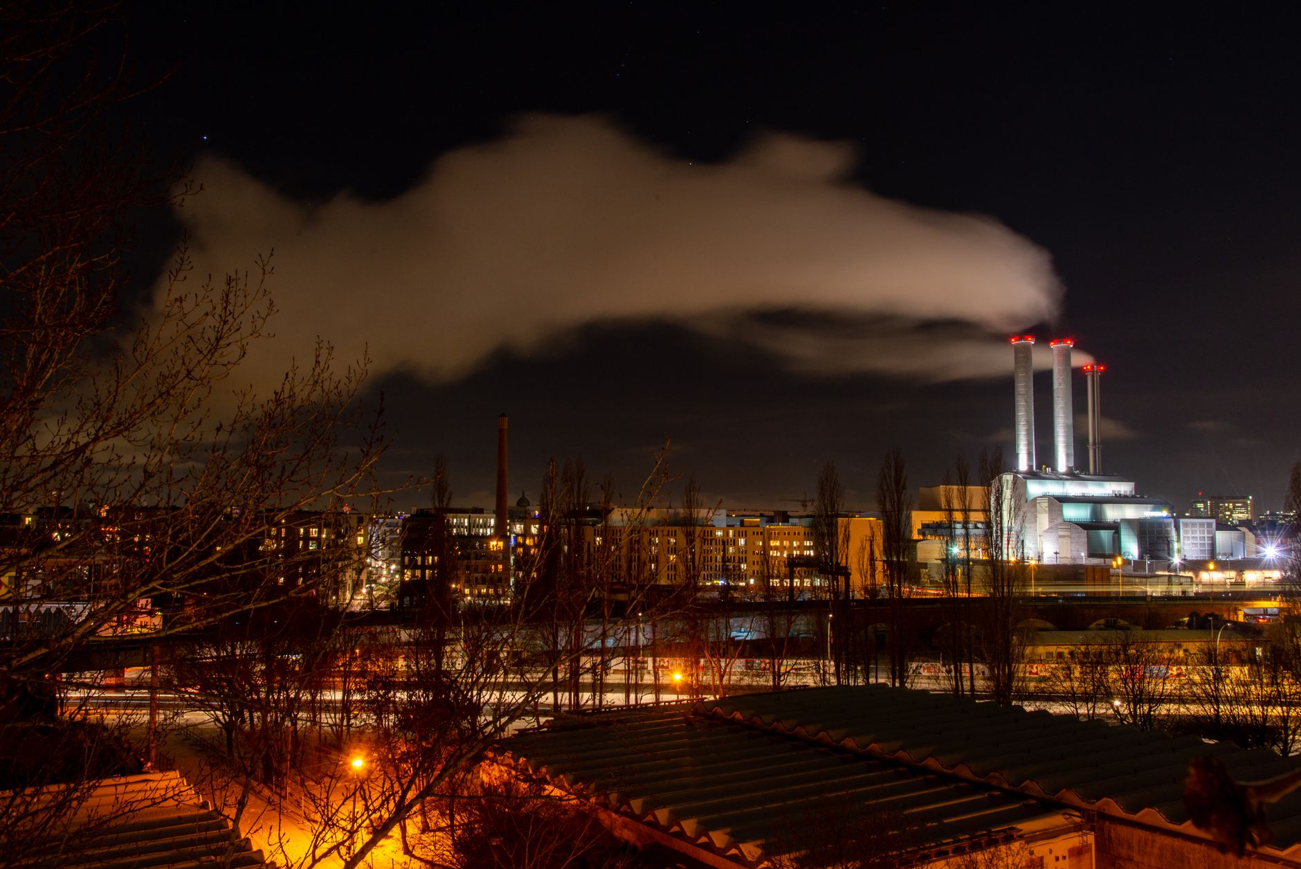 A vibrant city at night featuring an industrial power plant emitting smoke under a starry sky.
