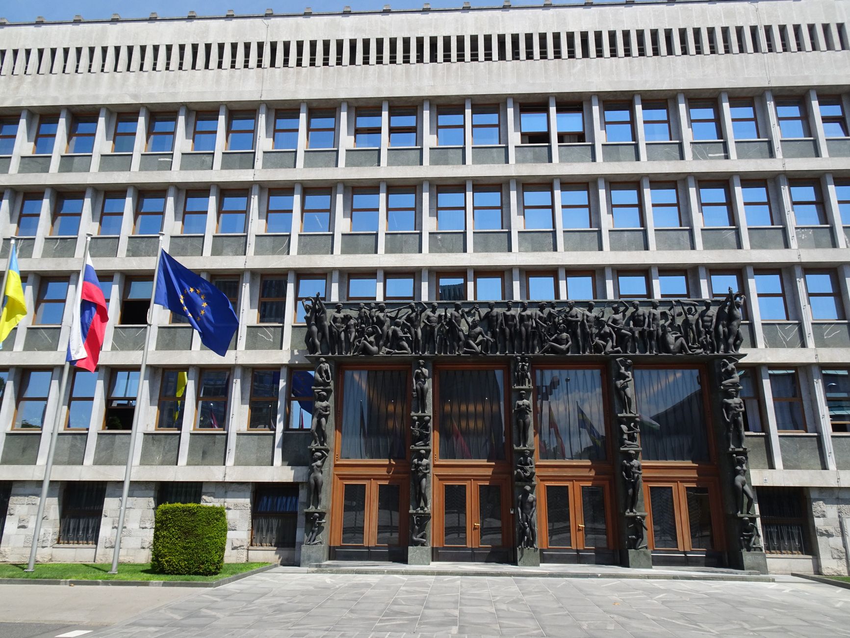 Front view of the Slovenian Parliament Building in Ljubljana with flags and sculptures. Bright summer day.