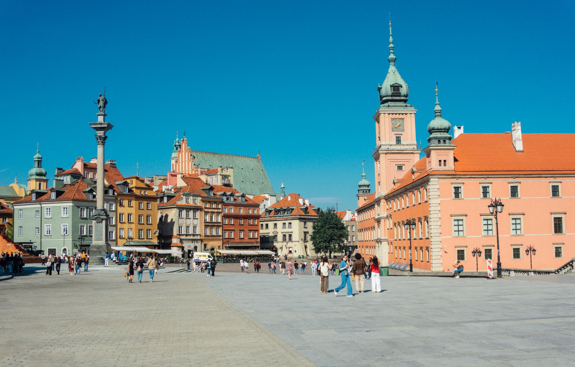 Vibrant Warsaw Old Town Square with colorful historic buildings and tourists enjoying a sunny day.