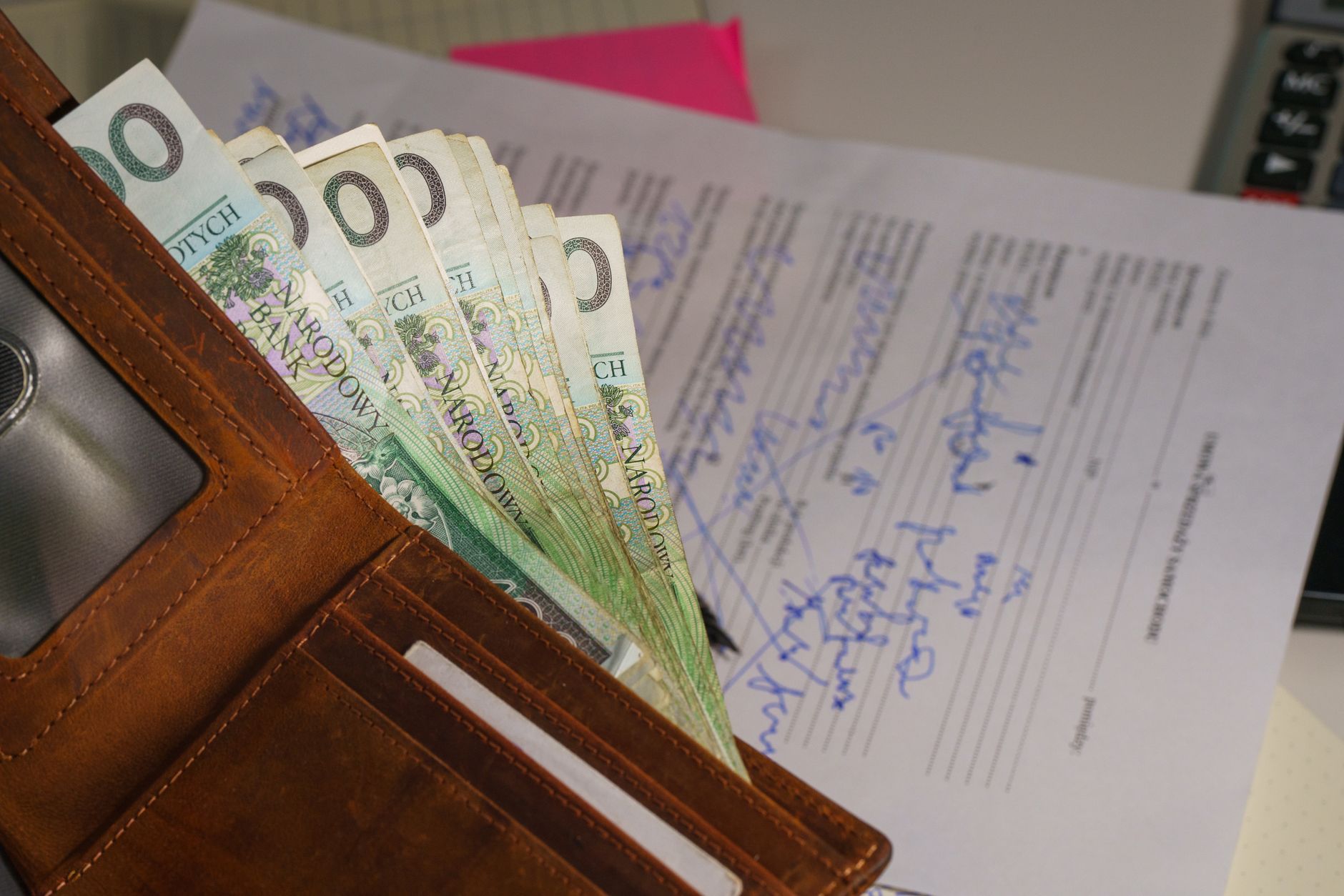 Close-up of a wallet containing Polish Zloty with a signed document in the background, representing financial transactions.