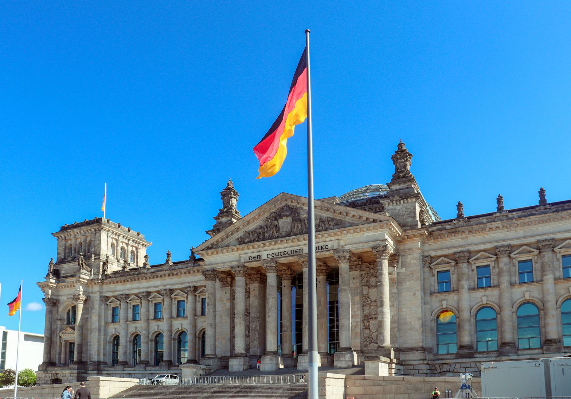 Reichstag building in Berlin with German flag against a clear blue sky during the day.