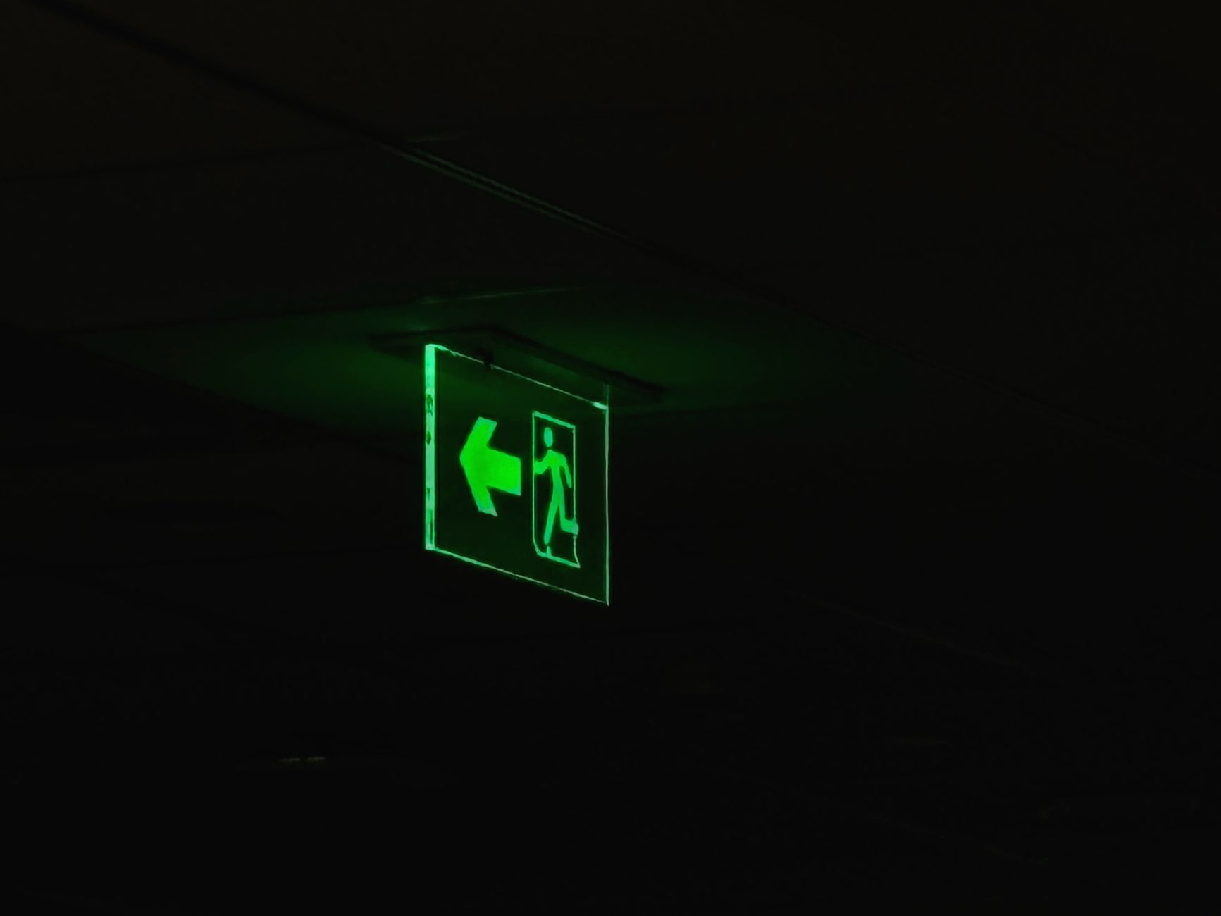 An illuminated green emergency exit sign with directional arrow in a dark setting.