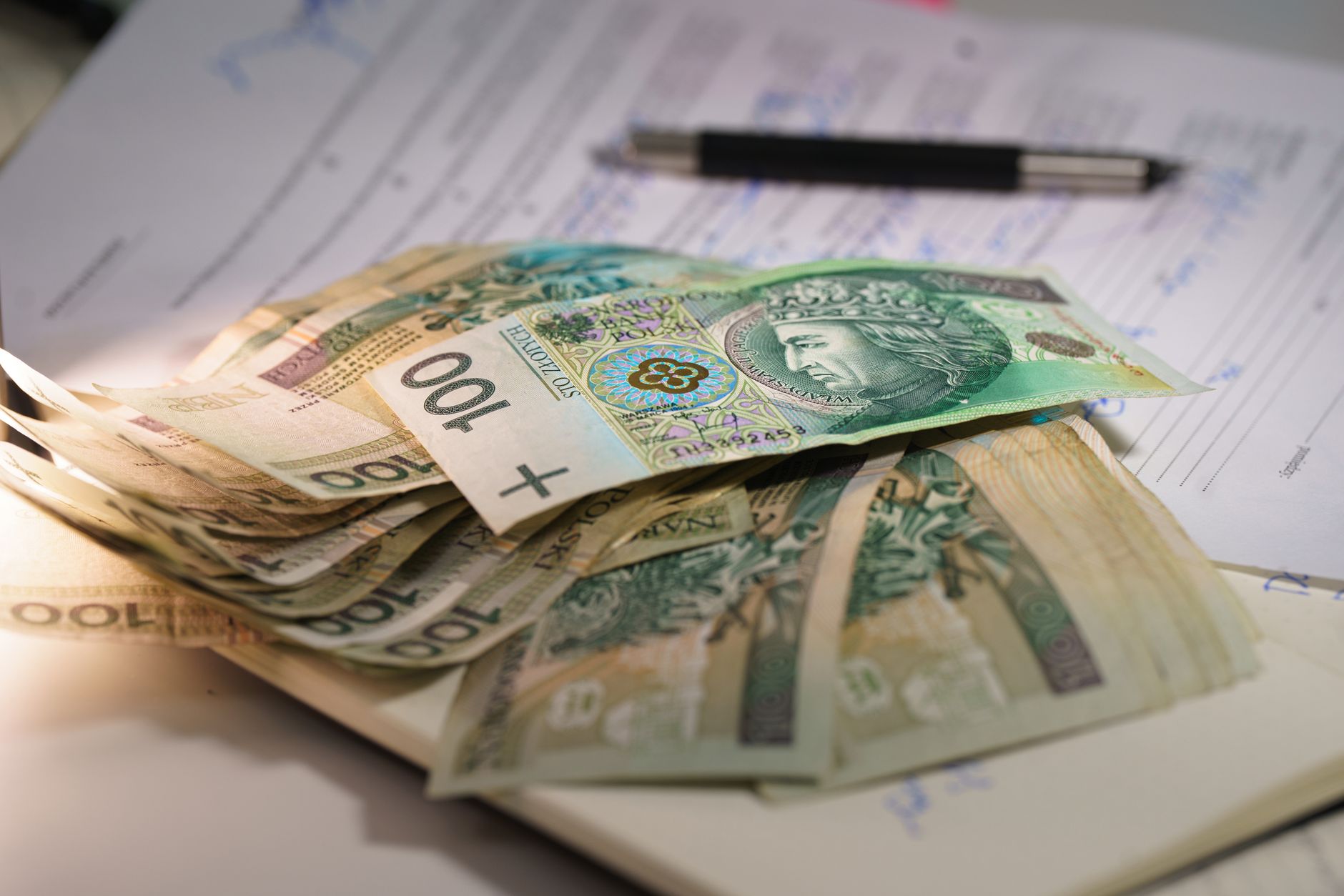 Stack of Polish zloty banknotes on financial documents with a pen, indicating monetary transactions in an office setting.