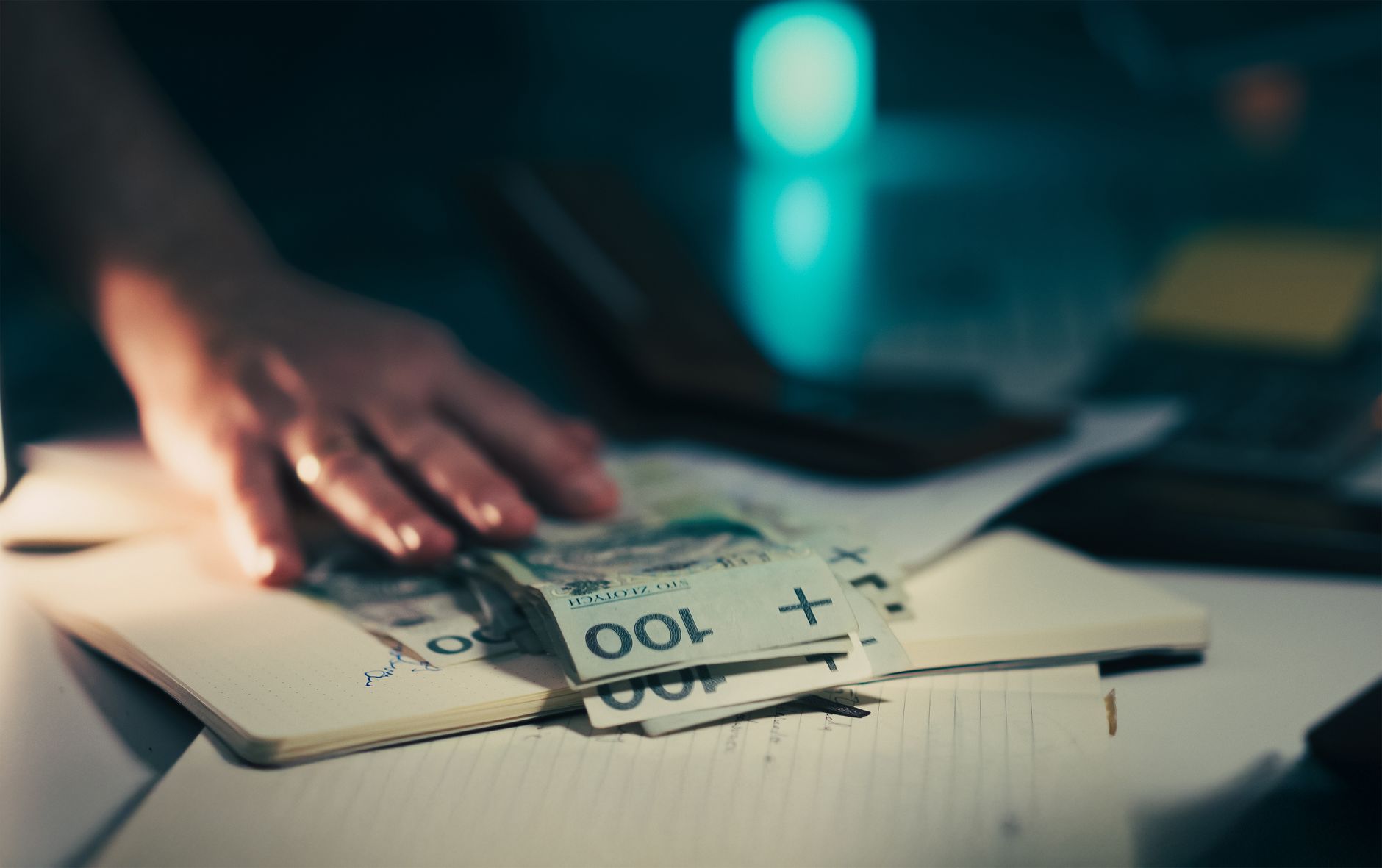 Close-up of hand reaching for banknotes on an office desk with a notebook and calculator.