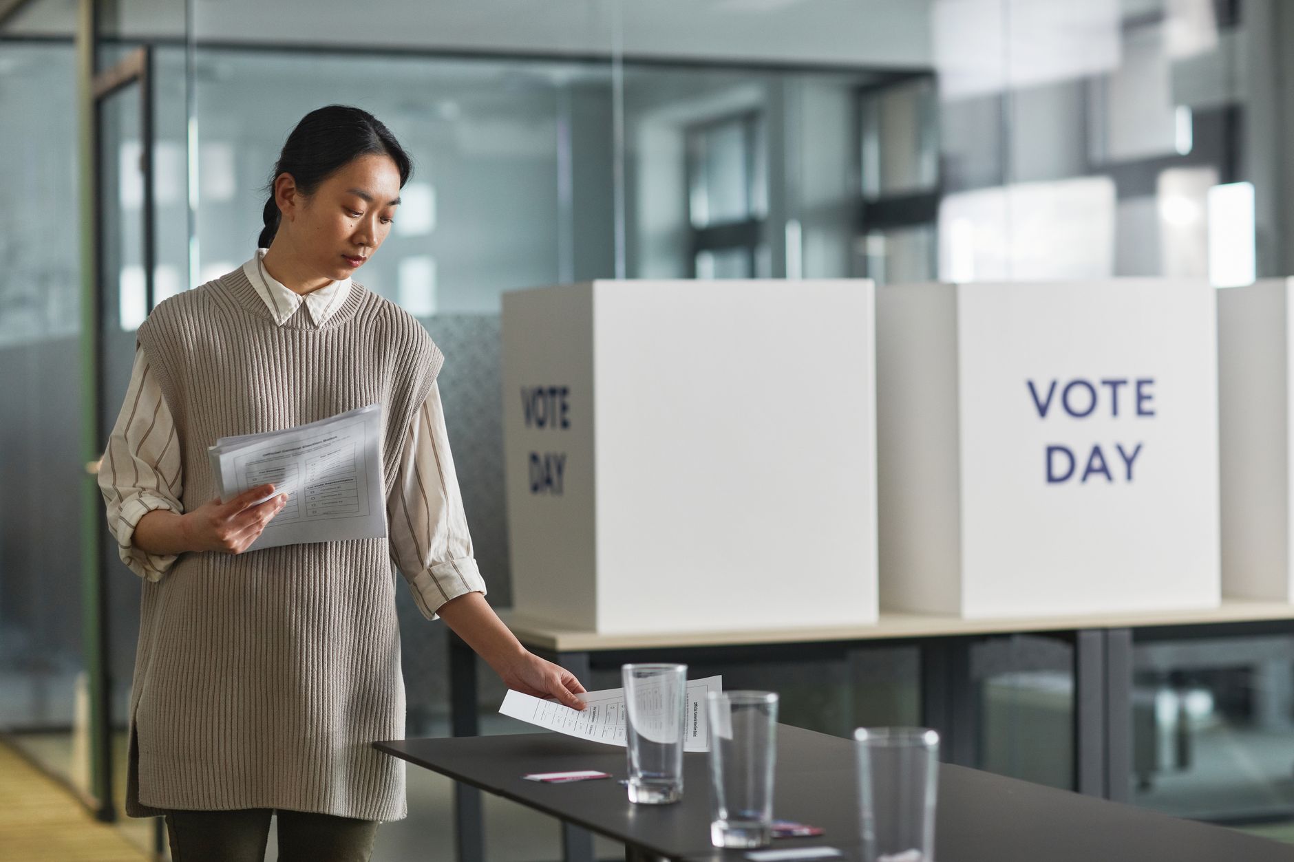 A woman organizing ballot papers indoors at a voting station on election day.