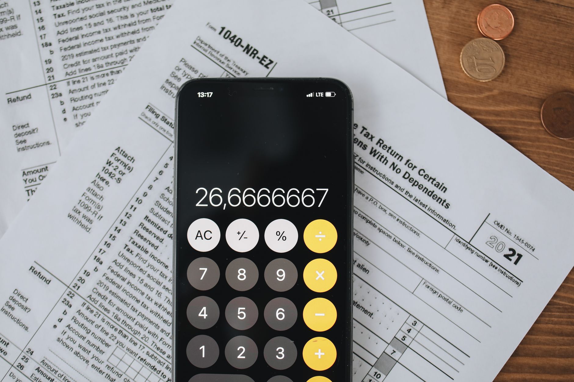 Smartphone calculator over tax forms with coins, symbolizing tax calculation and finance.